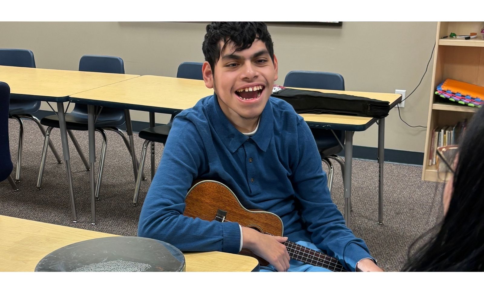 A smiling teen holding a ukulele at the studio