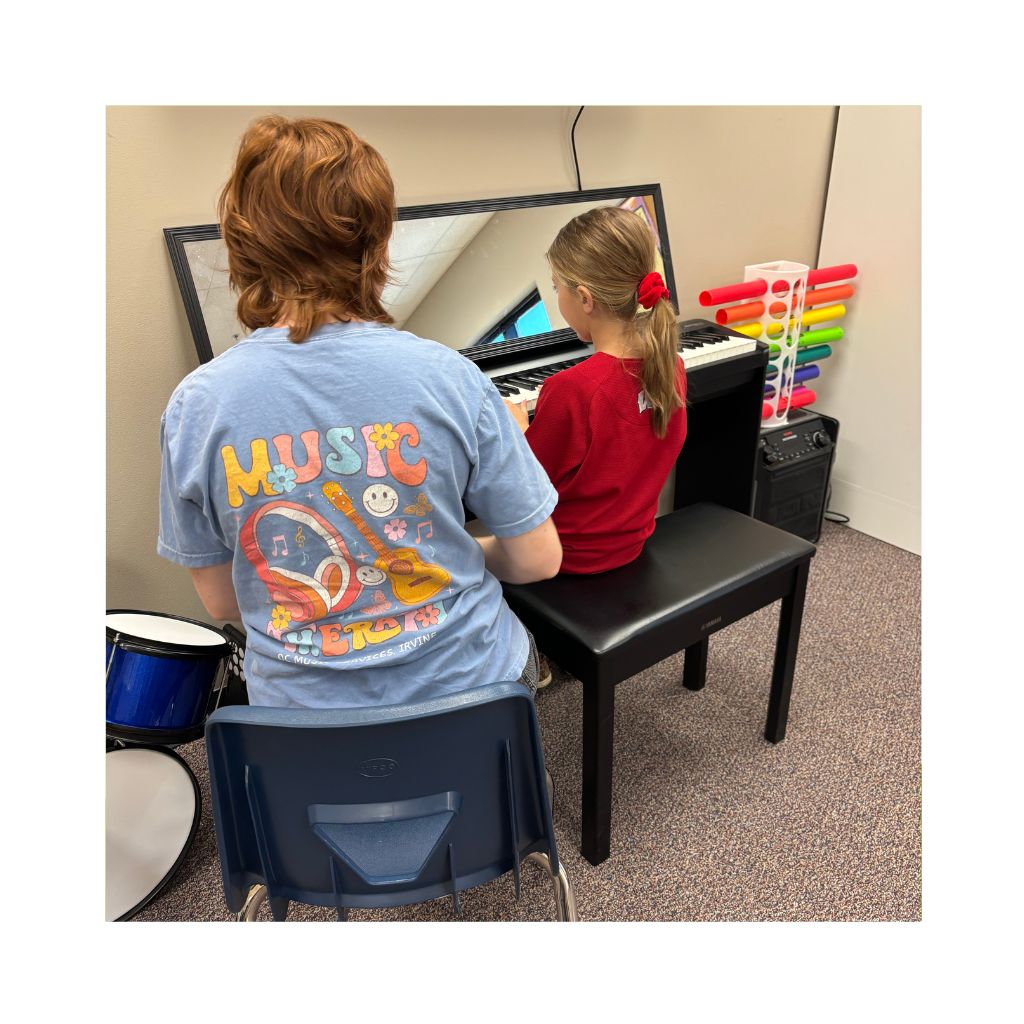 Board-certified music therapist supporting a young child at the piano during a music therapy session in Orange County, serving Norwalk and Anaheim Hills, California. Colorful percussion instruments and a drum set are visible in the therapy room.