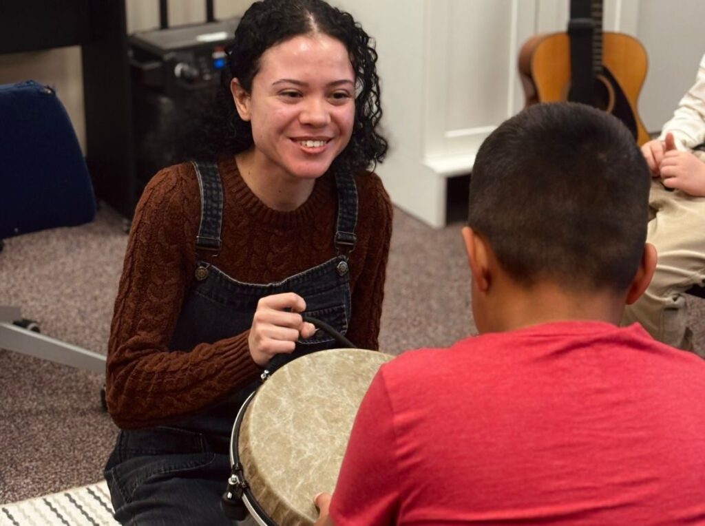 orange county california Music therapist smiling and engaging with a young boy during a drumming activity in a music therapy session, supporting social and motor skill development in a warm, supportive environment.