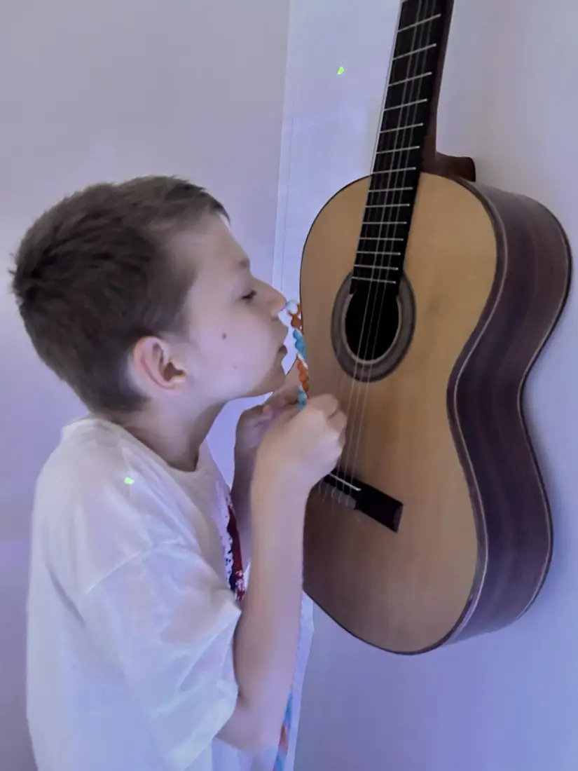 A young student leans in close to strum an acoustic guitar