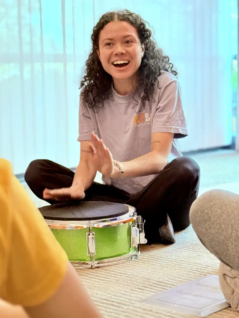 A smiling teacher playing a bright green snare drum with her hands