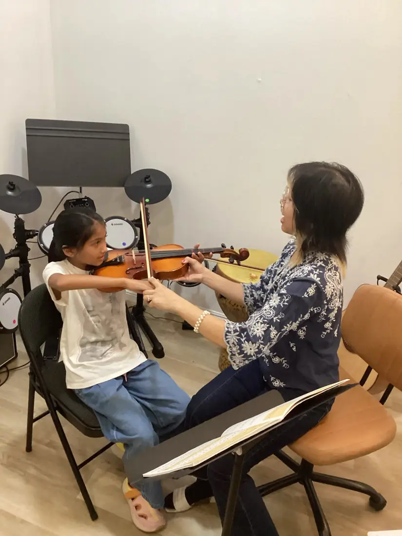 A teacher helping a student hold a violin bow