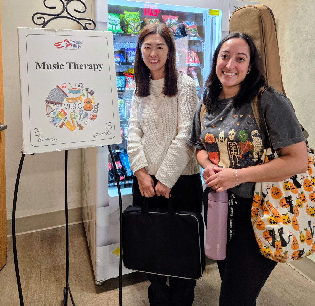Two OC Music Services music therapists at Freedom Village next to the music therapy sign