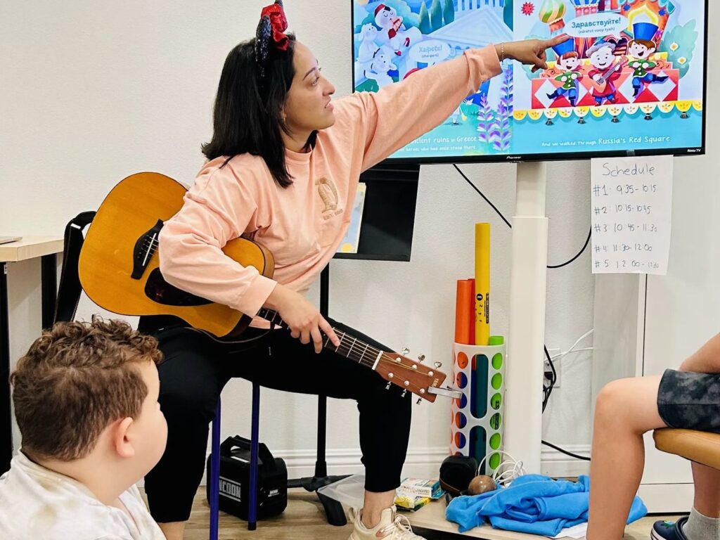 A teacher with a guitar leads a group music class at OC Music Services in Santa Ana