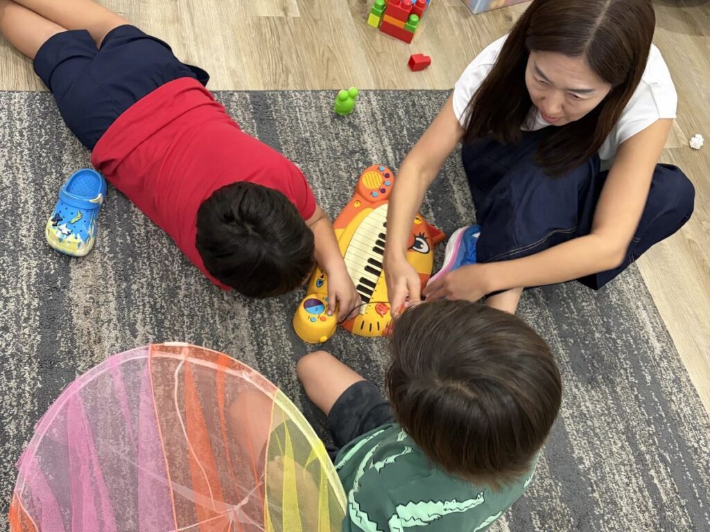 Two young students playing a keyboard with their teacher in a group music class