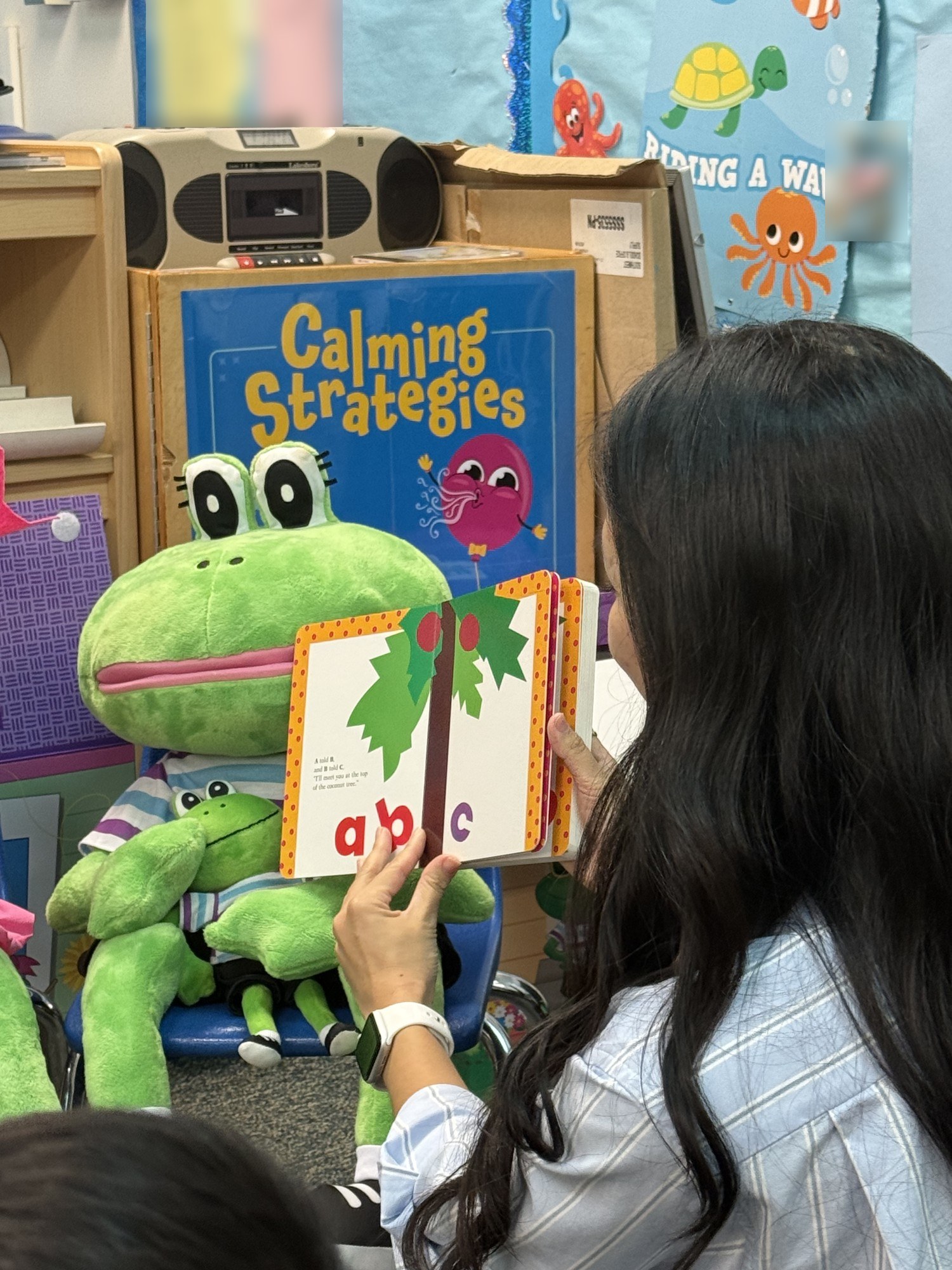 A teacher holding up an ABC book next to a frog puppet