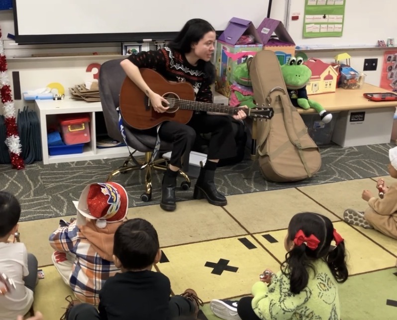 An OC Music Services teacher playing guitar for a circle of preschoolers
