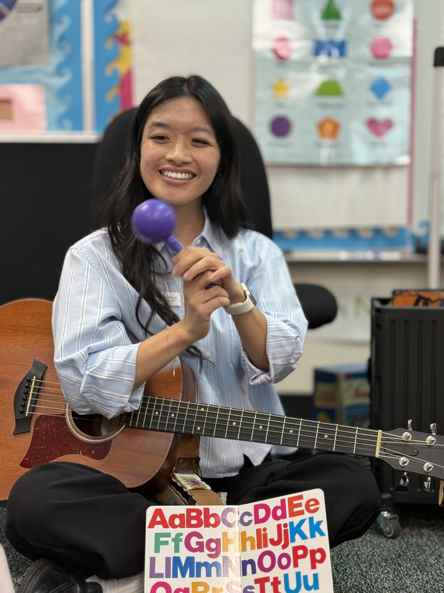 A smiling OC Music Services teacher holding a shaker and guitar