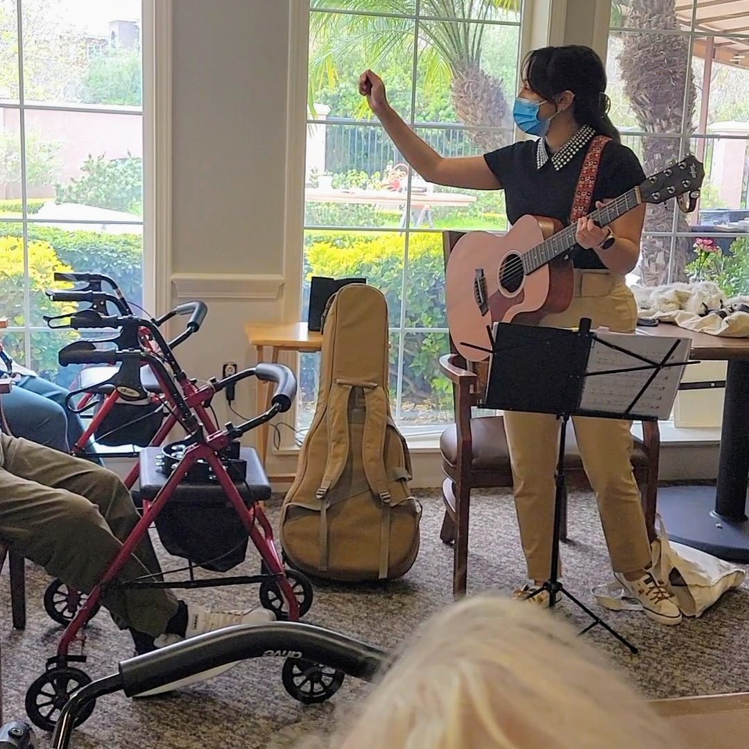 An OC Music Services music therapist leading a group sing along with guitar for senior residents