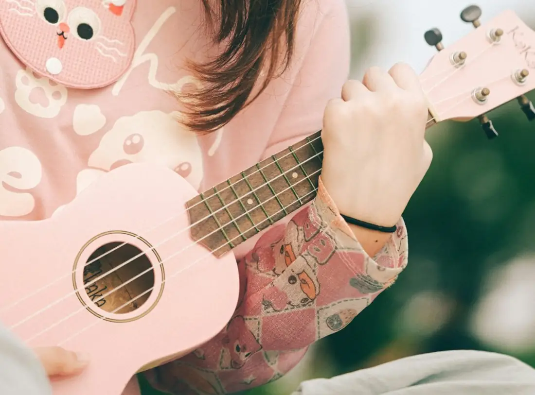 Close up of hands playing a pink ukulele